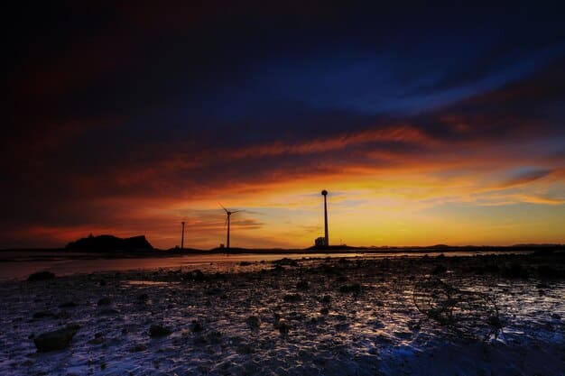 An elevated view of an offshore wind farm at sunset, with towering wind turbines rising from the sea, their blades silhouetted against the colorful sky.