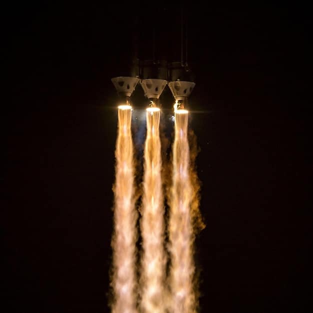 A launch sequence of a reusable rocket, capturing the dramatic ascent from the launchpad. Flames engulf the base as the rocket powers upwards, with the Earth's curvature visible in the background. The image conveys the power and cost-effectiveness of reusable launch technologies.