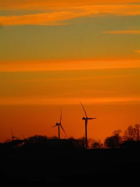 A wind farm at sunset, illustrating renewable energy infrastructure. The image captures the scale and technological advancement of wind power, with turbines silhouetted against a colorful sky.
