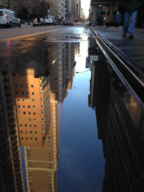 A flooded street in a coastal US city after a hurricane, with people wading through the water and damaged buildings in the background.