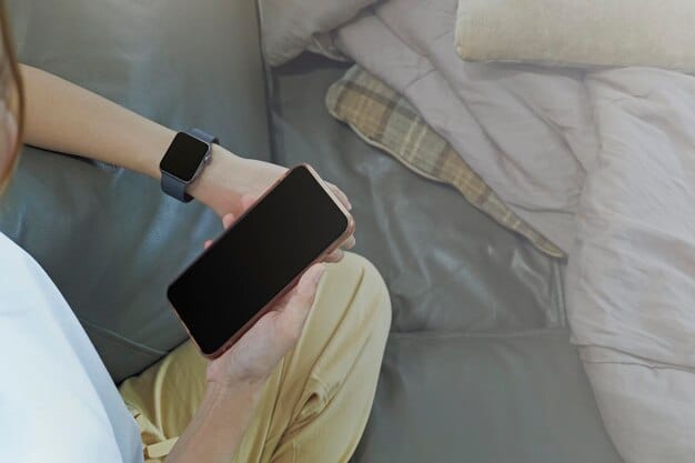 A person wearing a smartwatch in bed, with a smartphone displaying sleep tracking data next to them on the nightstand.