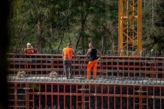 Construction workers on a bridge construction site, wearing hard hats and reflective vests, with heavy machinery in the background, showcasing the on-the-ground activity fueled by infrastructure investments.