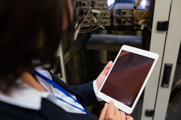 A close-up shot of a technician using a tablet to monitor and adjust the settings of a robotic arm on a manufacturing assembly line. The focus is on the digital interface and the technician's interaction with the technology.